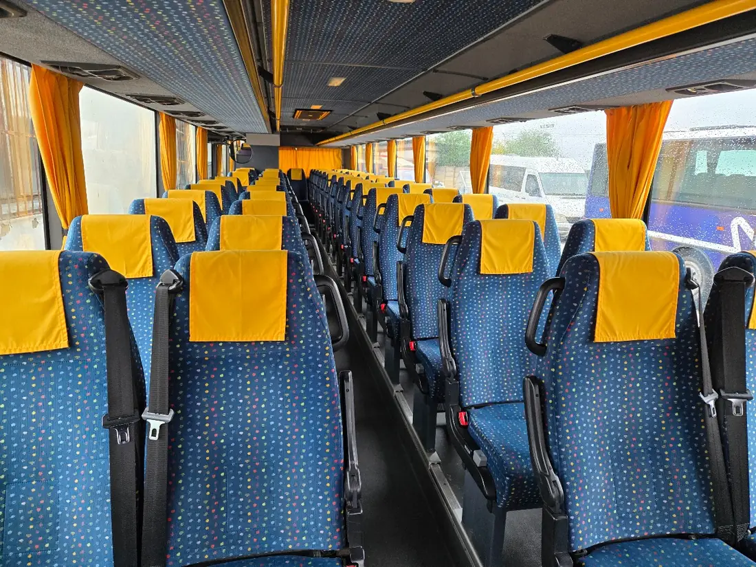 Interiér autobusu s modrými sedadly se žlutými opěrkami hlavy a žlutými závěsy