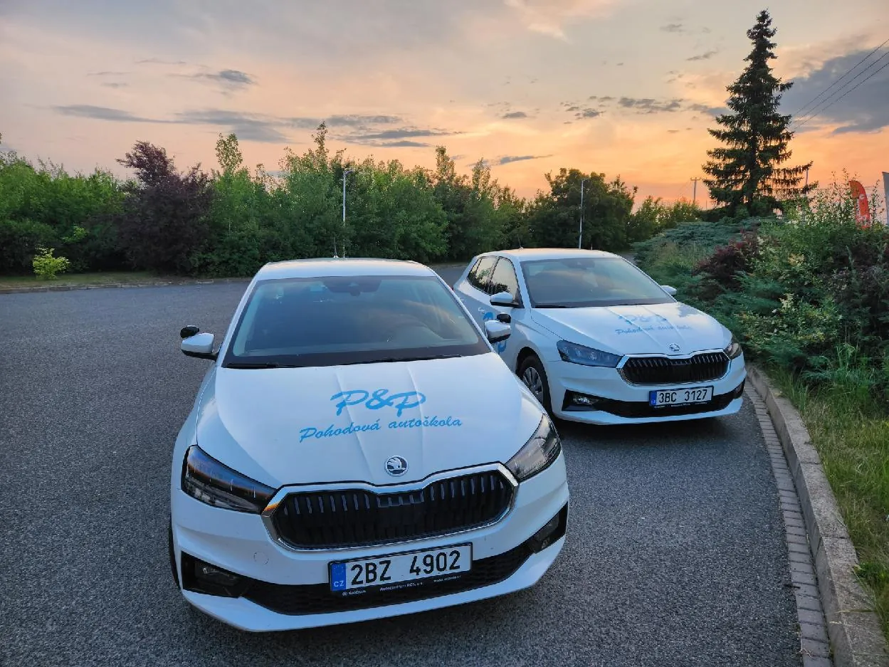 Dvě bílé výcvikové Škody Fabia s logem P&P Pohodová autoškola na parkovišti při západu slunce