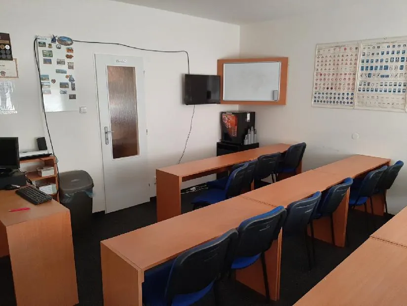 Učebna autoškoly: lavice s modrými židlemi, televize, bílá tabule a tabule s dopravními značkami na stěně
